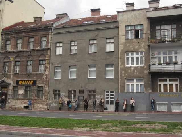 Workers waiting for a bus in Sarajevo. Note the patched bullet holes in the wall (building second from the right). 