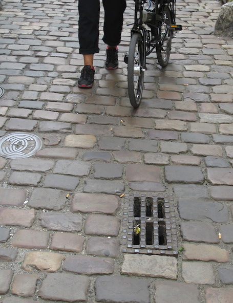 Cobblestones and a nasty grate, not designed for cyclists. In bike-friendly countries the slots are ‘S’ shaped. 