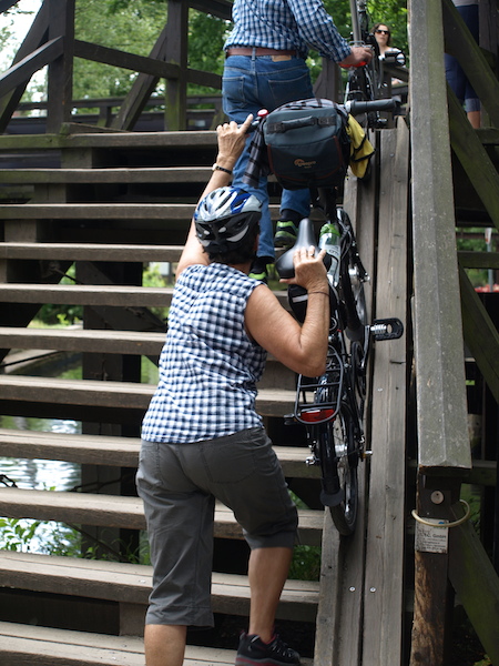 Bev pushing her bike up and over. Tourists don’t do this! Each raised bridge has a ramp in which the bike wheels go and once in position all you do is push. 