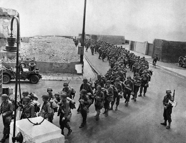 American soldiers, equipped with full pack and an extra allotment of ammunition, march down an English street to their invasion craft for embarkation to Normandy. Image credit: AP from http://vcepinc.org