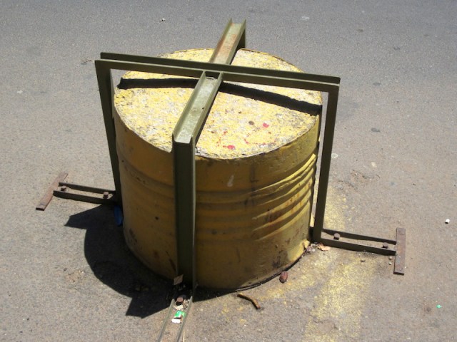 A No Parking deterrent, a half oil drum full of concrete bolted to the road. The drum deterrents extended right along the front of a building. 