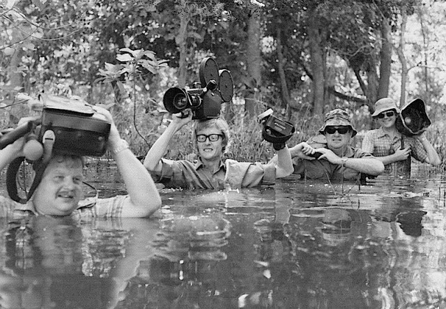 Ted with camera on his head wading across a creek in New Guinea. 